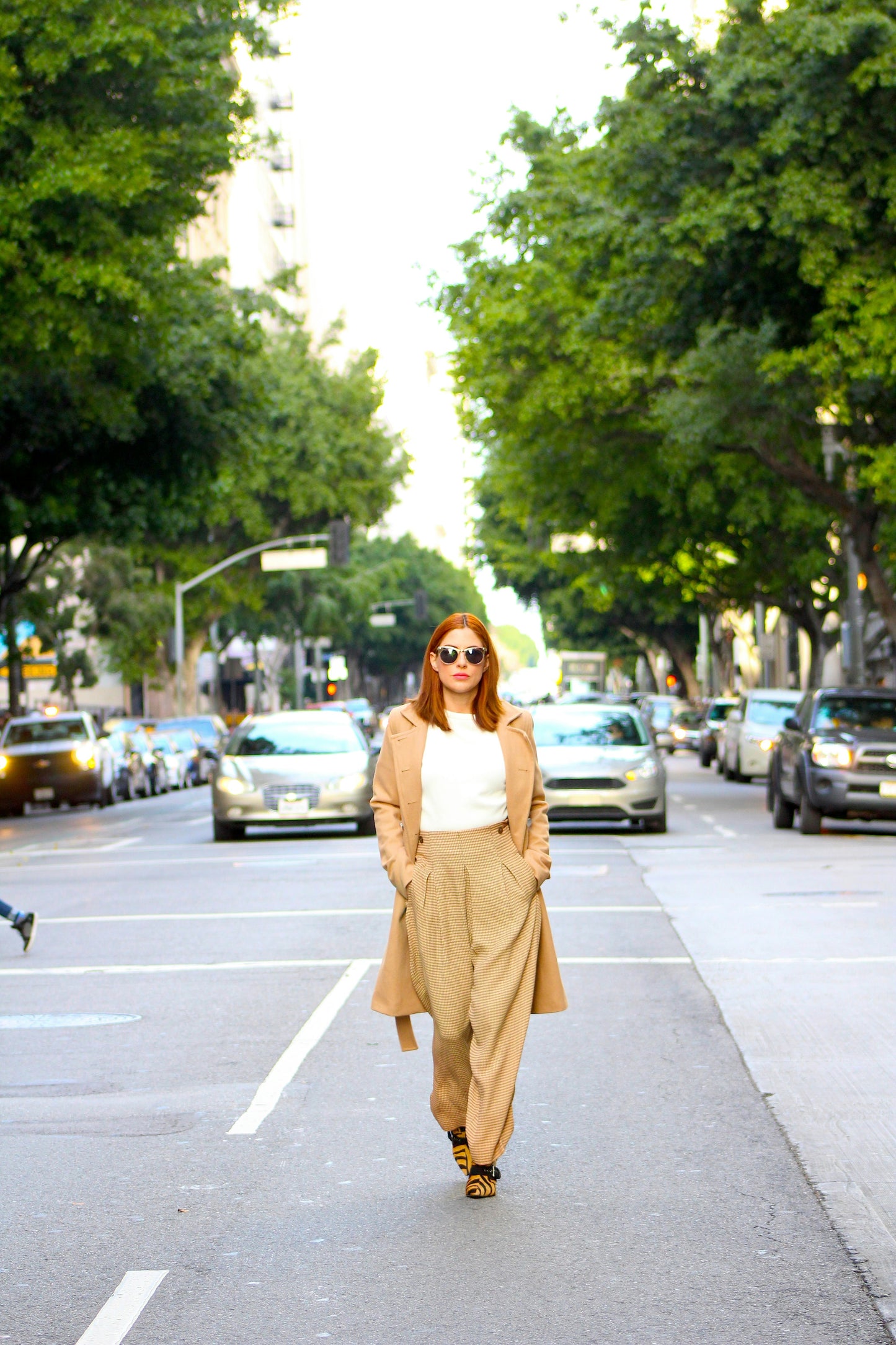 Woman walking on a city street with trees and cars in the background