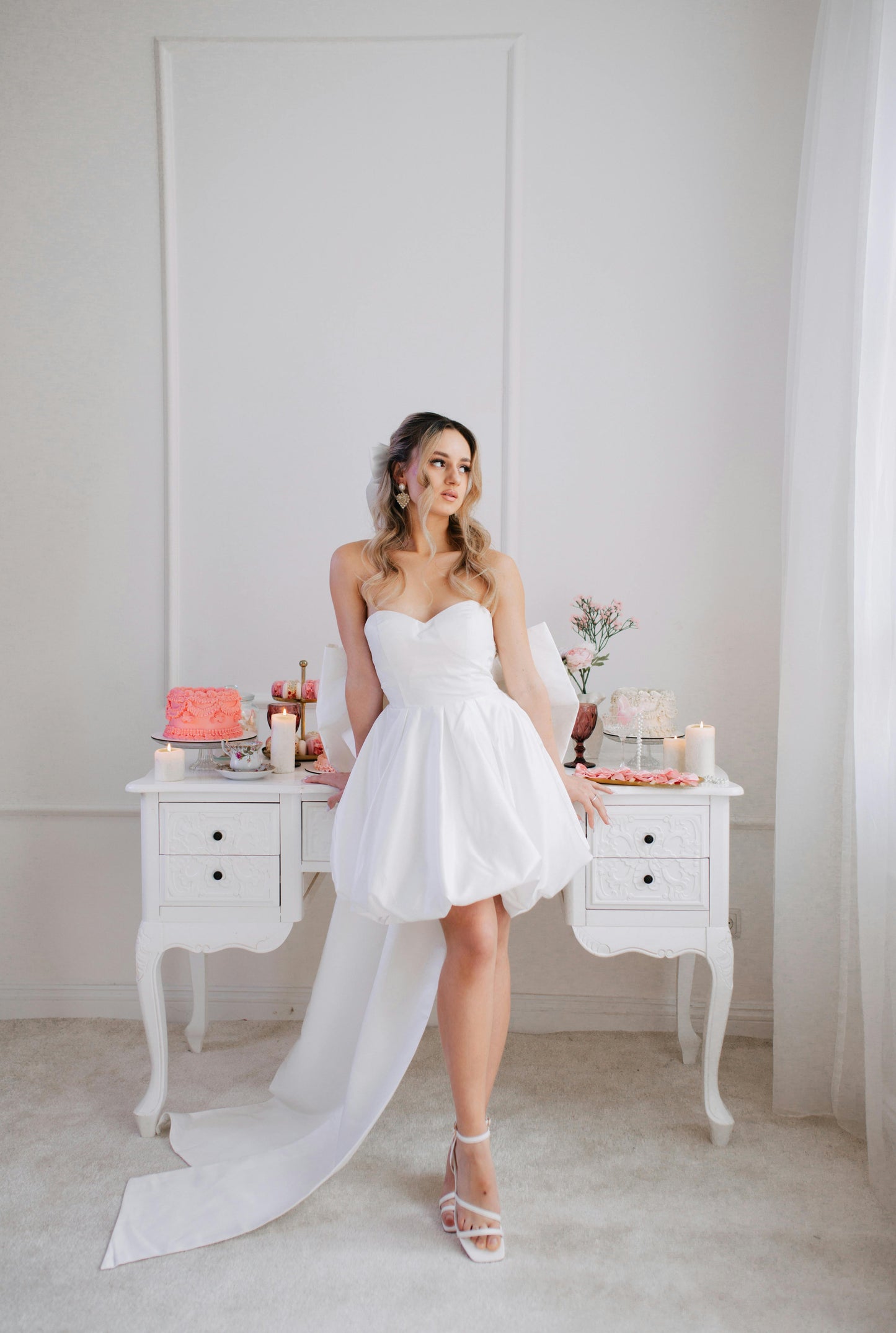 Woman in a white strapless dress standing in a room with a table and decorative items.