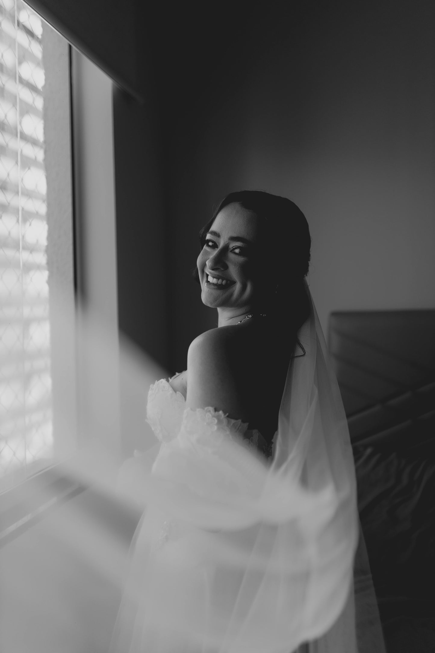 Black and white photo of a bride standing by a window