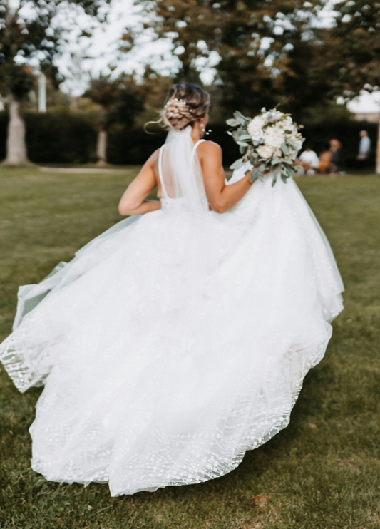 Bride running along grass field with bouquet