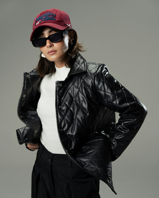 Person wearing a black quilted jacket, white shirt, dark pants, sunglasses, and a red cap on a gray background