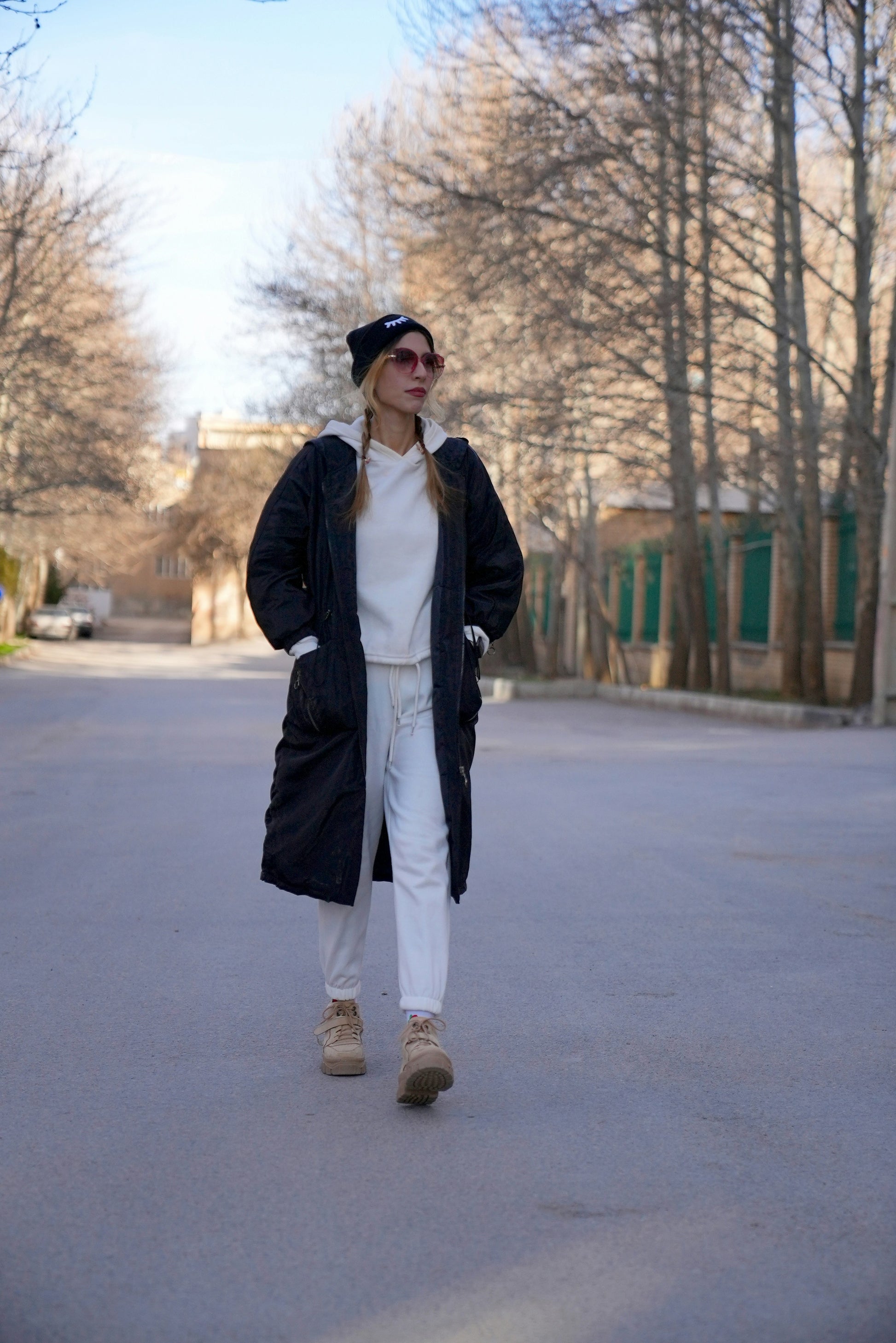 Person walking on a street wearing a black coat, white pants, and beige boots.
