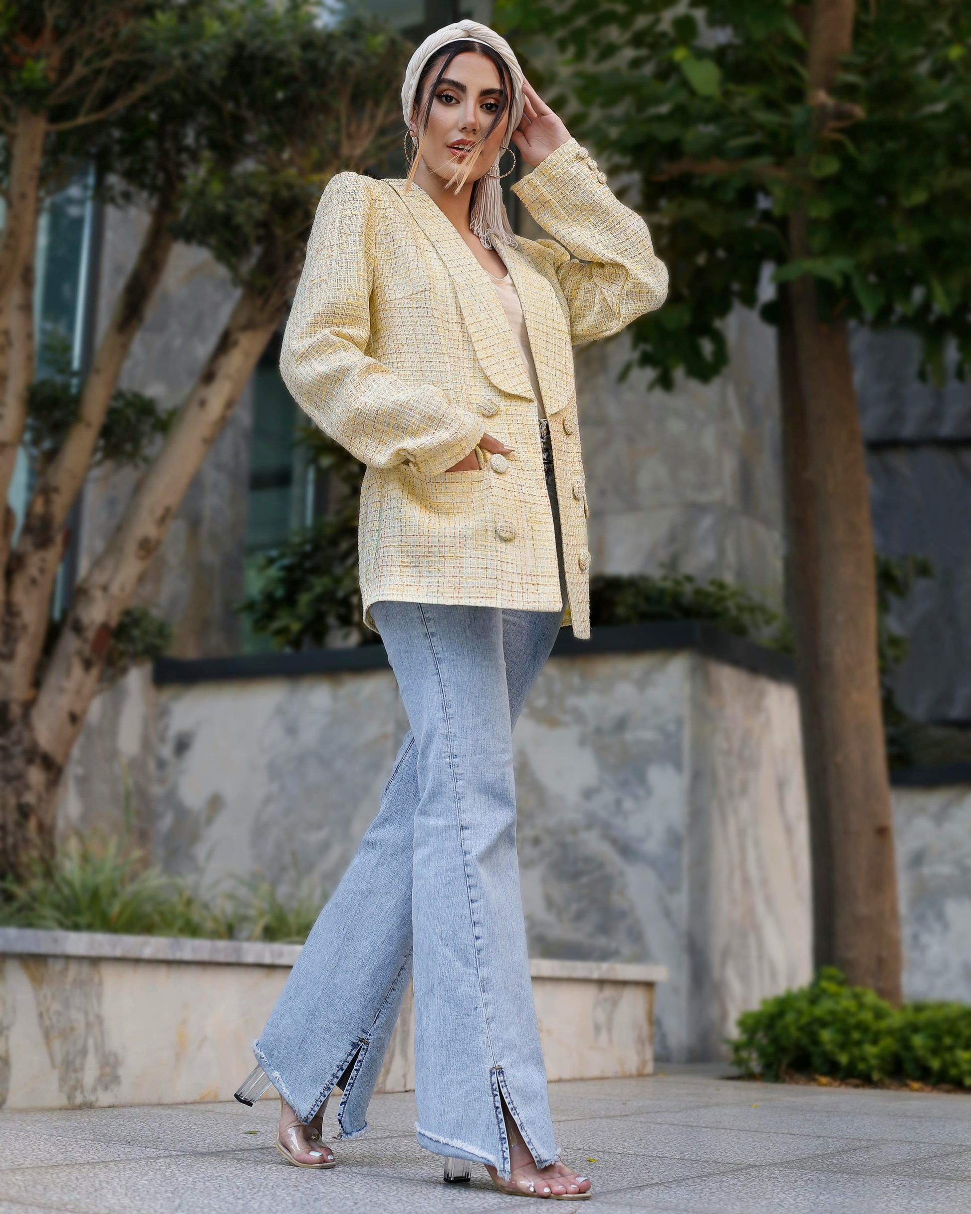 Woman wearing a light yellow blazer and light blue jeans outdoors.