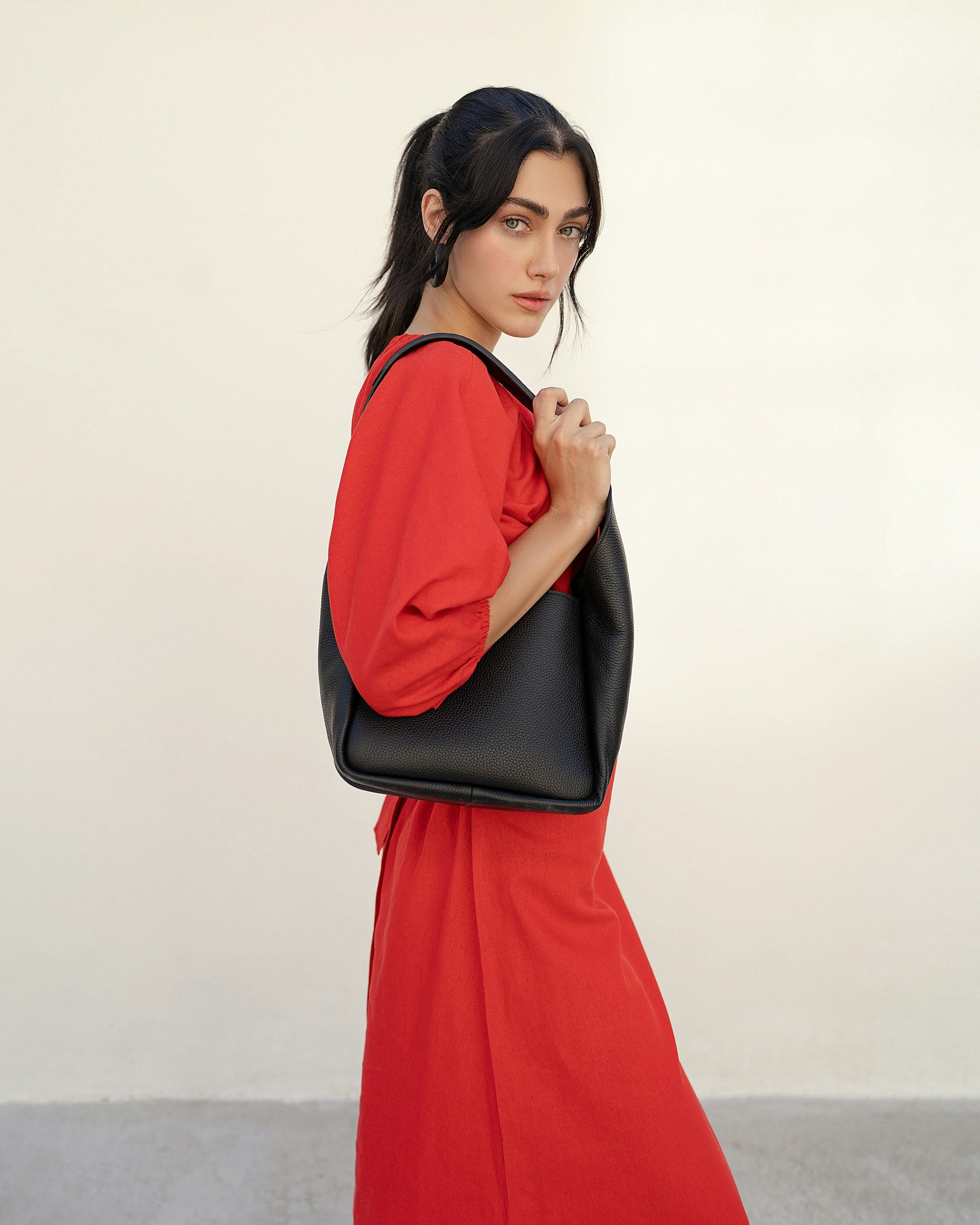 Woman in a red dress holding a black bag against a plain background