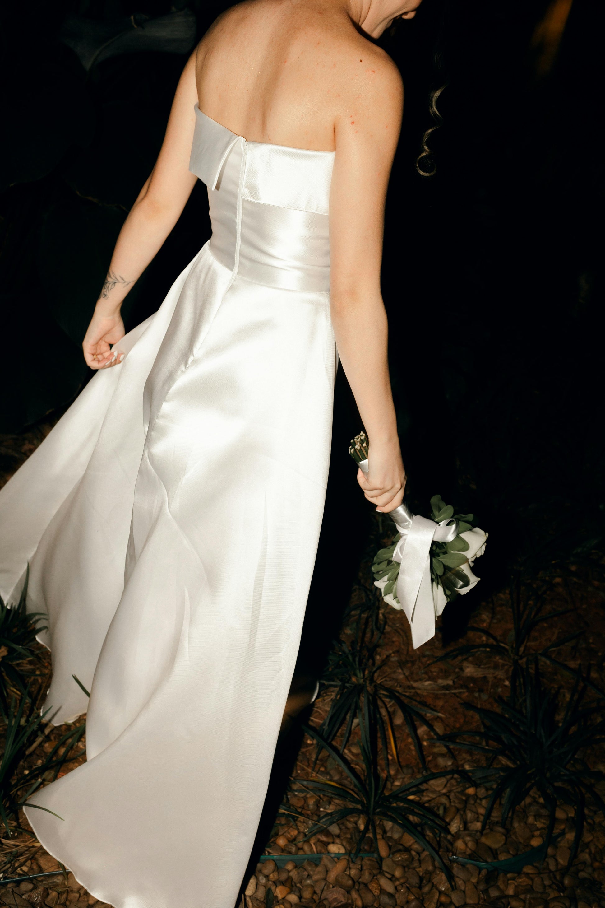 White strapless gown with a person holding a bouquet in a dark setting