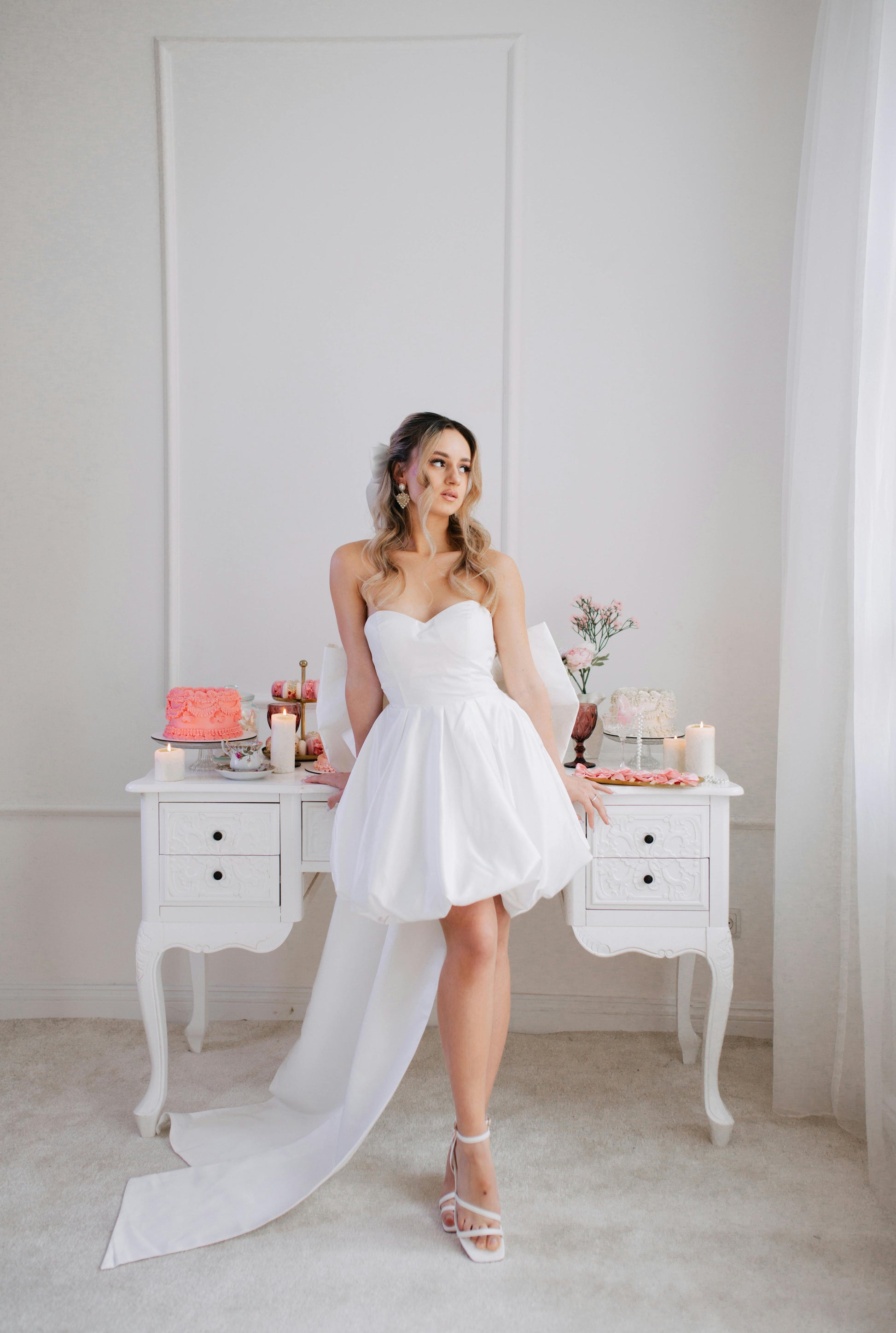 Woman in a white strapless dress standing in a room with a table and decorative items.