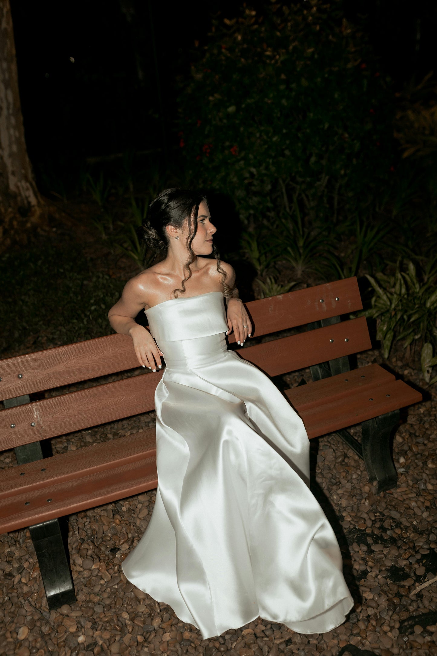 Woman in a white dress sitting on a wooden bench at night.