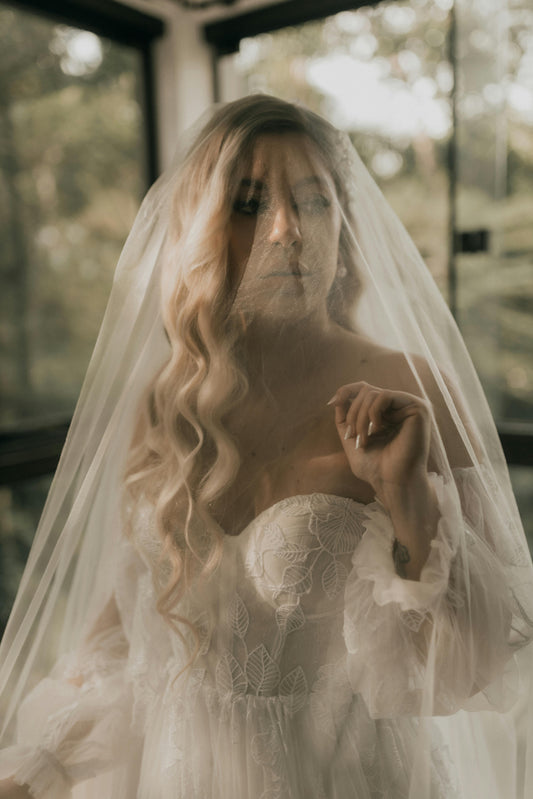 Woman in a wedding dress with a veil, standing indoors with blurred background