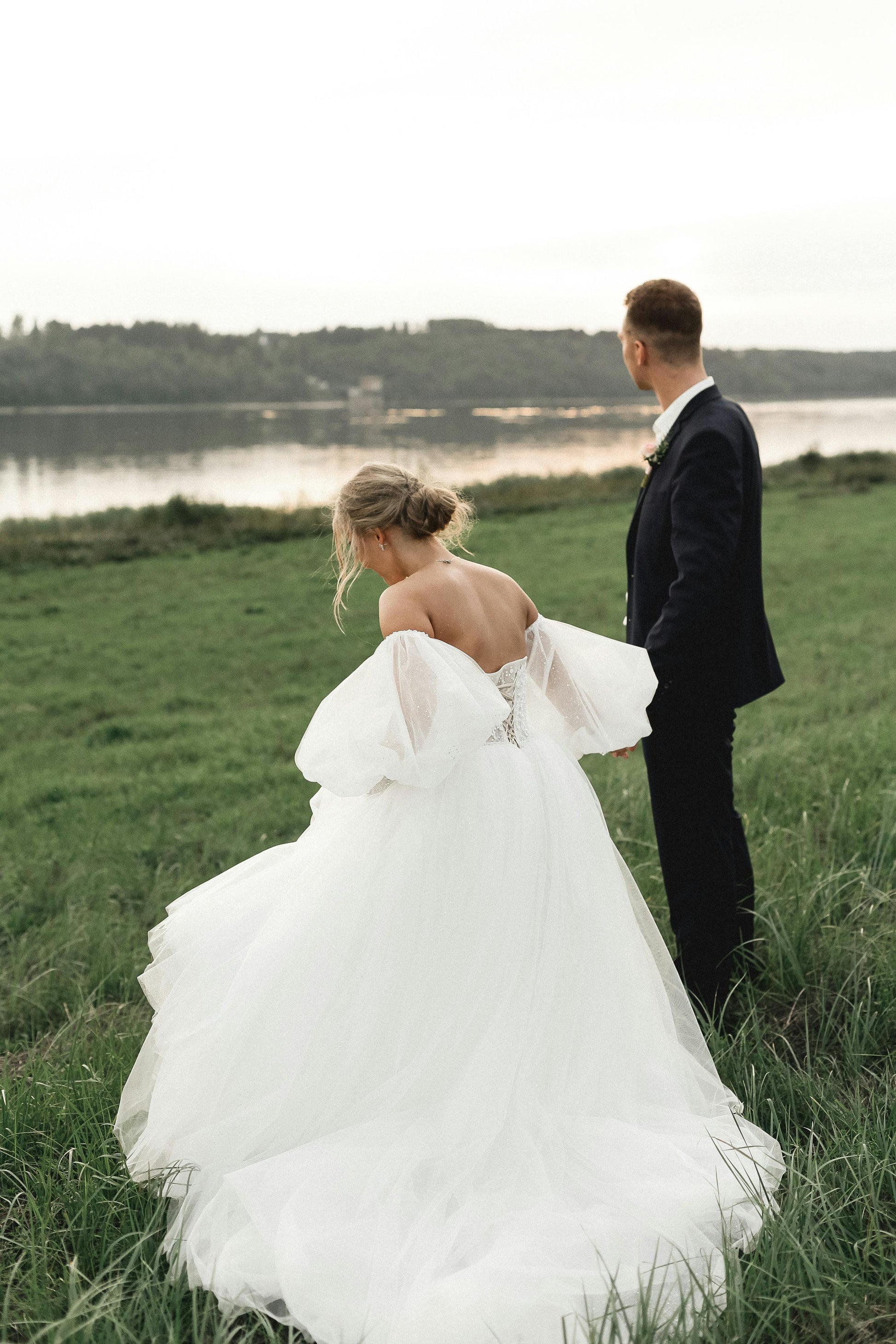 Couple standing in a grassy field with a lake in the background