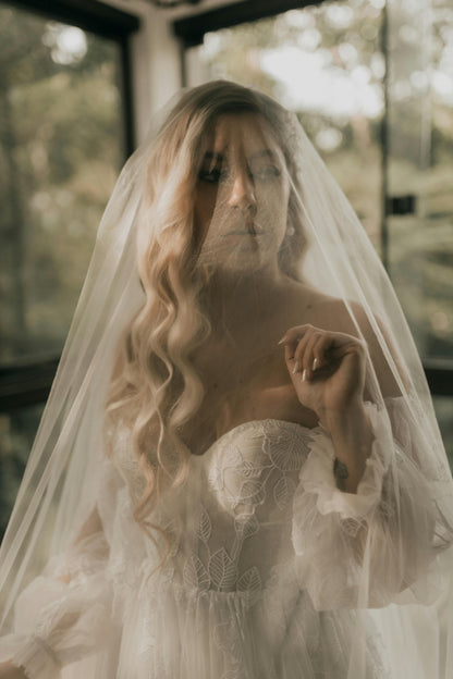 Woman in a wedding dress with a veil, standing indoors with blurred background. Victoria Ellison is a Fashion Stylist specialising in Bridal Styling, Pregnancy Styling, Motherhood Styling, Personal Styling.