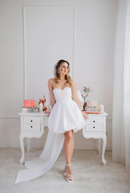 Woman in a white strapless dress standing in a room with a table and decorative items. Victoria Ellison is a Fashion Stylist specialising in Bridal Styling, Pregnancy Styling, Motherhood Styling, Personal Styling.