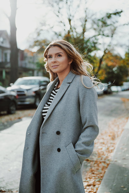 Woman wearing a gray coat standing on a street with trees and cars in the background. Victoria Ellison is a Fashion Stylist specialising in Bridal Styling, Pregnancy Styling, Motherhood Styling, Personal Styling.