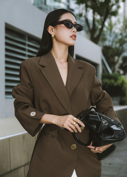 Woman in a brown suit holding a black handbag outdoors. Victoria Ellison is a Fashion Stylist specialising in Bridal Styling, Pregnancy Styling, Motherhood Styling, Personal Styling.